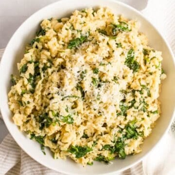 Close up of a white serving bowl full of brown rice mixed with wilted spinach and topped with Parmesan cheese.
