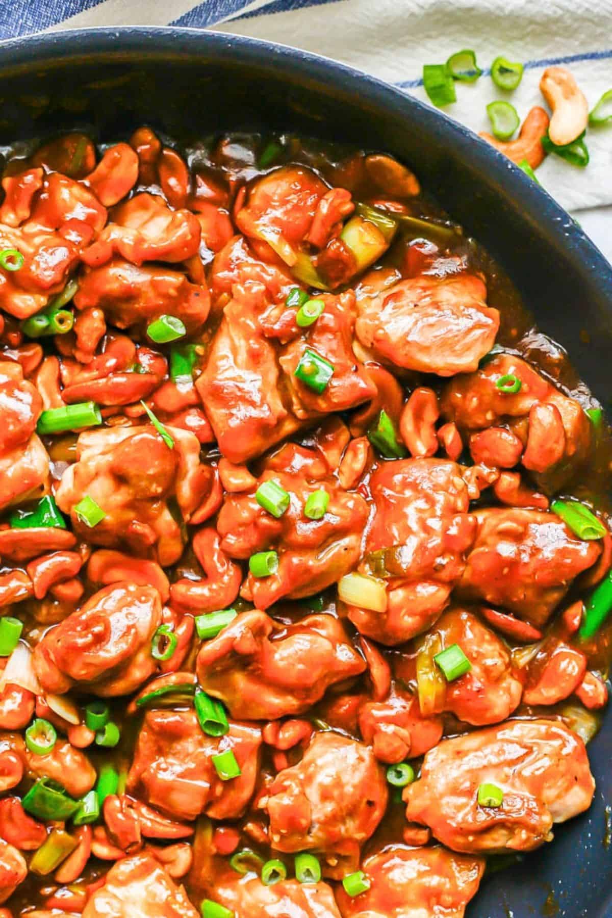 Cashew chicken is a 20-minute recipe with tender chicken pieces tossed in a garlicky light brown sauce with crunchy cashews and green onions. A skillet full of a homemade cashew chicken recipe with sliced green onions sprinkled on top.