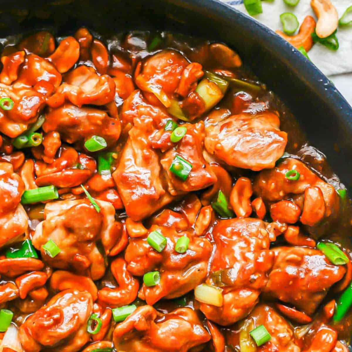 Close up of a skillet full of a homemade cashew chicken recipe with sliced green onions sprinkled on top.
