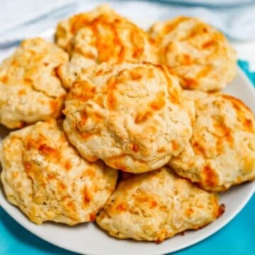 Close up of a white plate set on a teal napkin and piled with homemade cheddar garlic drop biscuits.