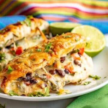 Close up of a chicken breast stuffed with cheese, black beans and tomatoes, with taco seasoning and cheese on top, served on a white plate.