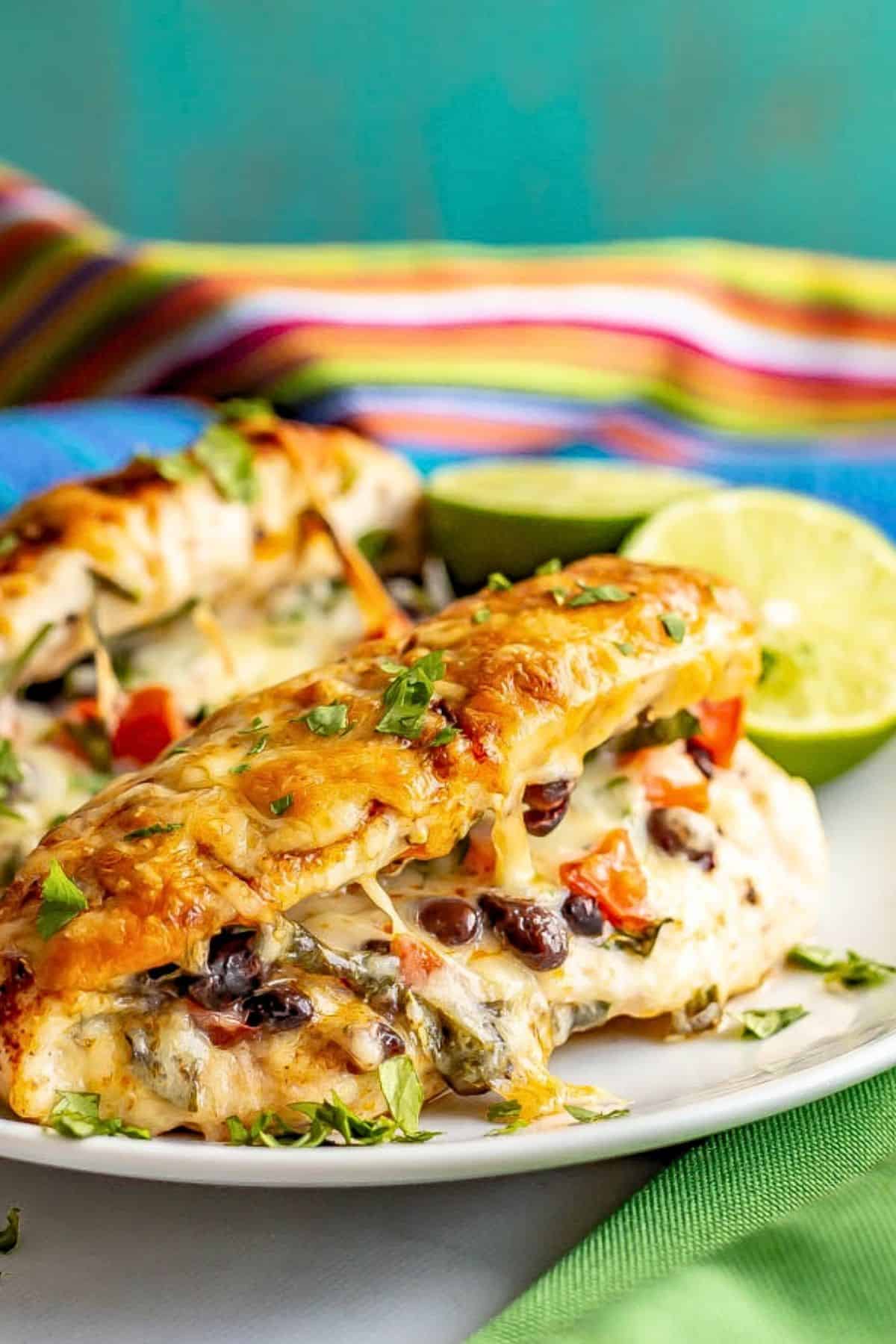 Two chicken breasts stuffed with cheese, black beans and tomatoes, with taco seasoning and cheese on top, served on a white plate.