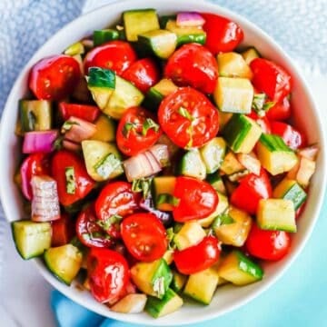 Close up of a white bowl filled with a mixed salad of cherry tomatoes, diced cucumber and chopped red onion in a balsamic vinaigrette.