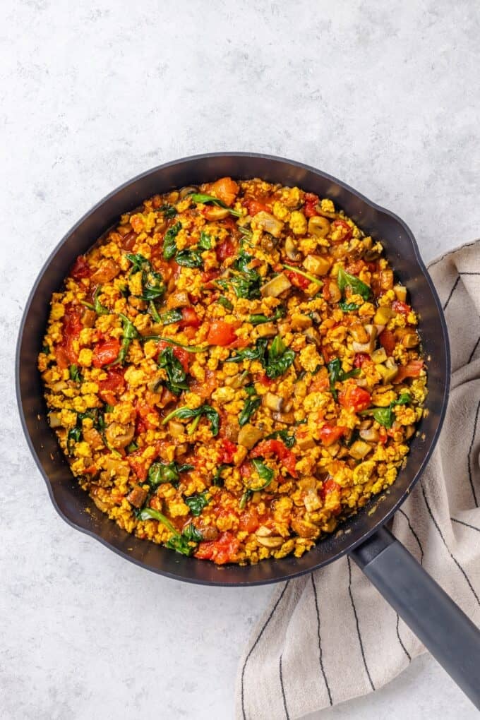 A large dark skillet with a curried ground chicken mixture with spinach and tomatoes.