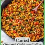 A wooden spoon resting in a large skillet filled with a curried ground chicken with mushrooms, spinach and tomatoes with a green border and text around the photo.