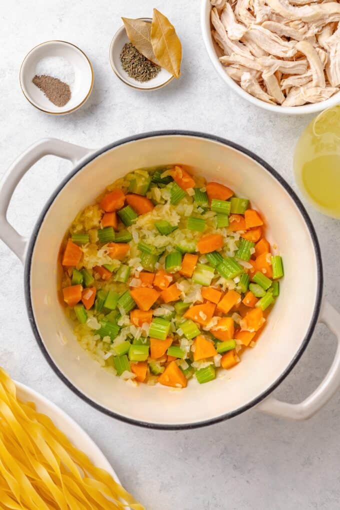 A large soup pot with sautéed onions, carrots, celery and garlic in it.