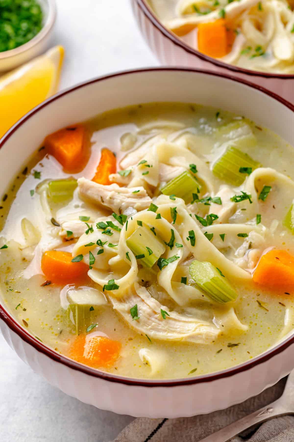 A serving bowl of chicken noodle soup with finely chopped fresh herbs sprinkled on top.