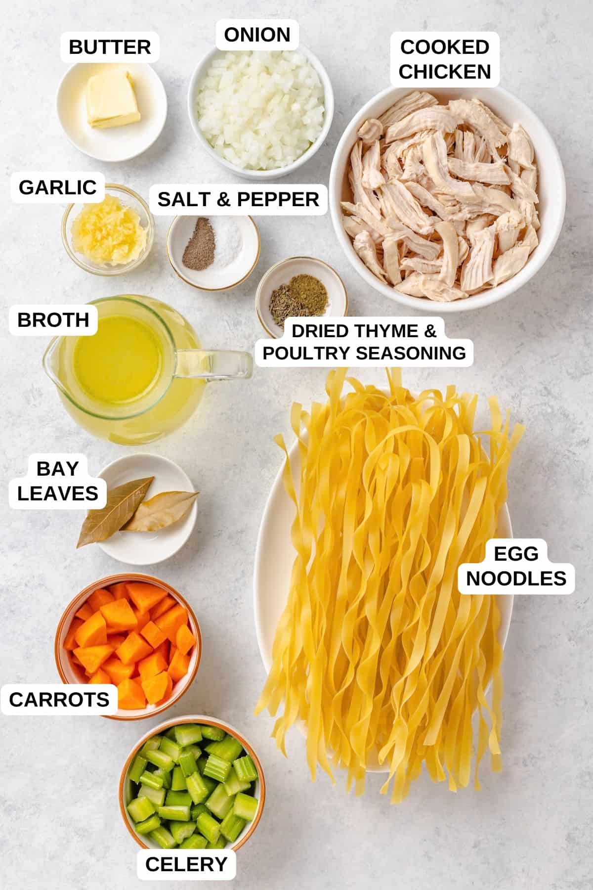 Ingredients laid out in separate bowls for making a chicken noodle soup with cooked chicken and egg noodles.