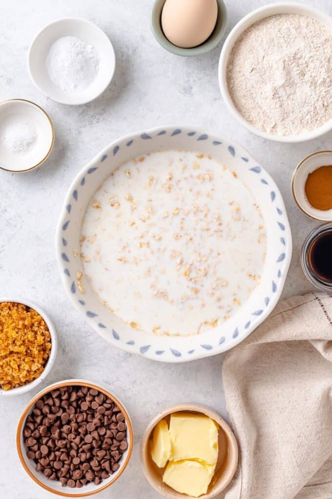 Oats soaking in milk in a bowl with bowls of other ingredients to the side.