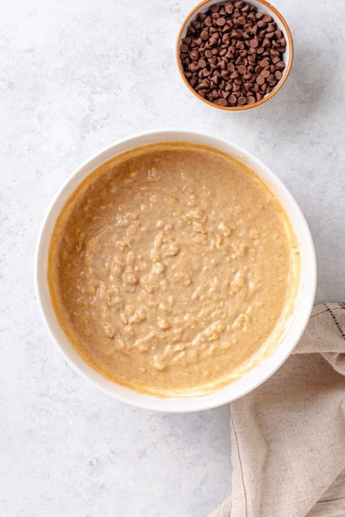 A healthy muffin batter in a white bowl with a bowl of chocolate chips to the side.