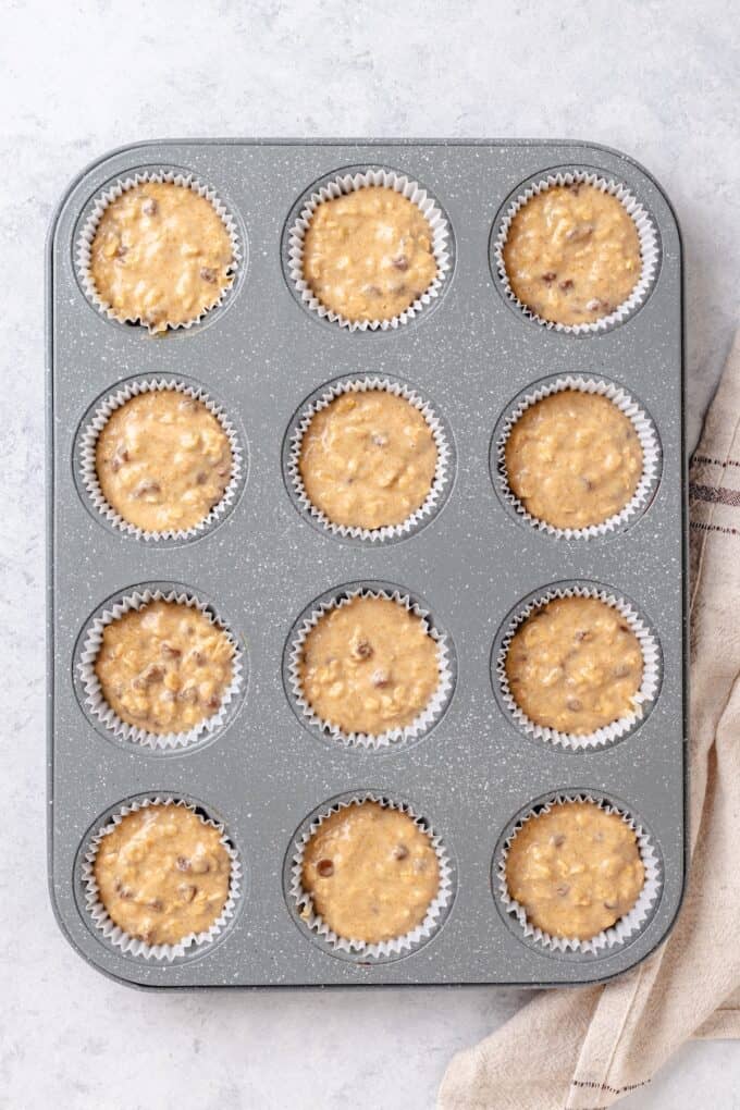 A muffin tin with muffin liners and a chocolate chip oatmeal muffin batter spooned into each one before baking.