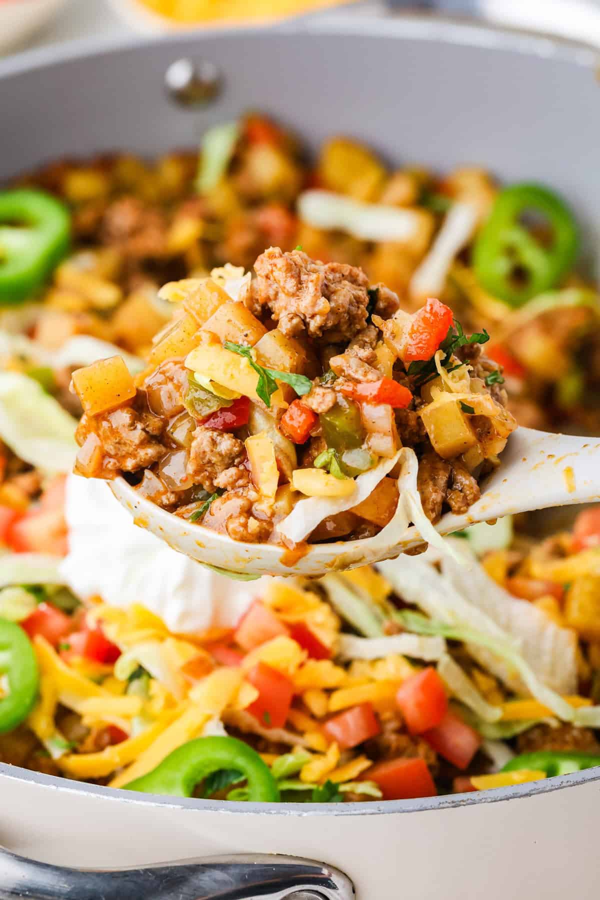 A spoon lifting out a scoop of a taco ground turkey and potato mixture from a large skillet.