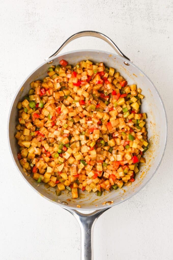A taco seasoned mixture of diced potatoes and peppers in a large skillet.