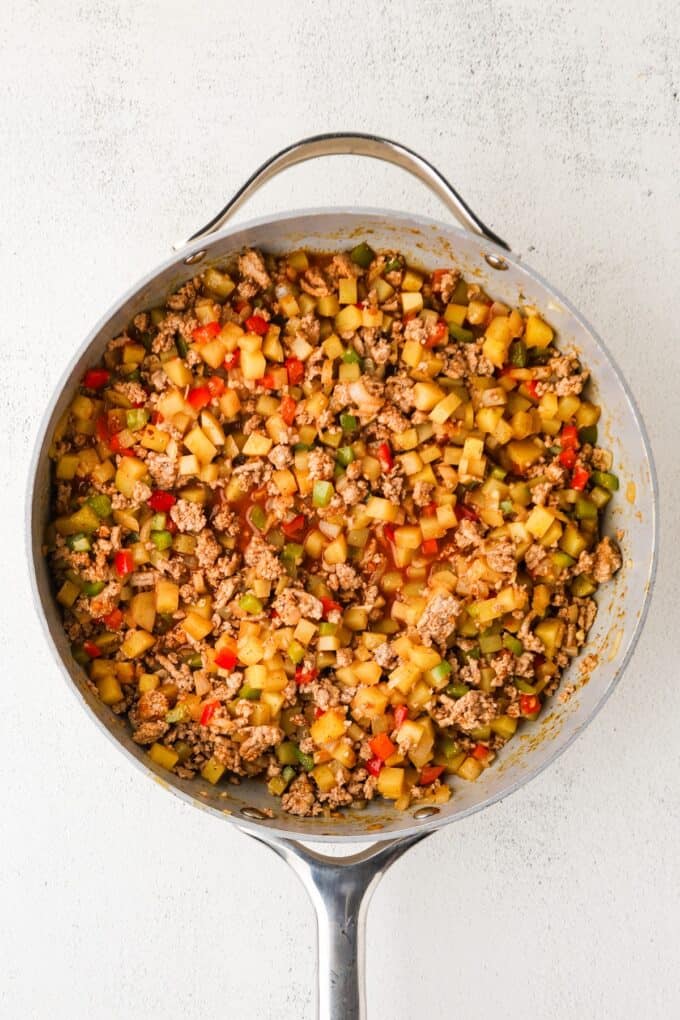 A large skillet full of ground turkey, potatoes and peppers with taco seasoning.