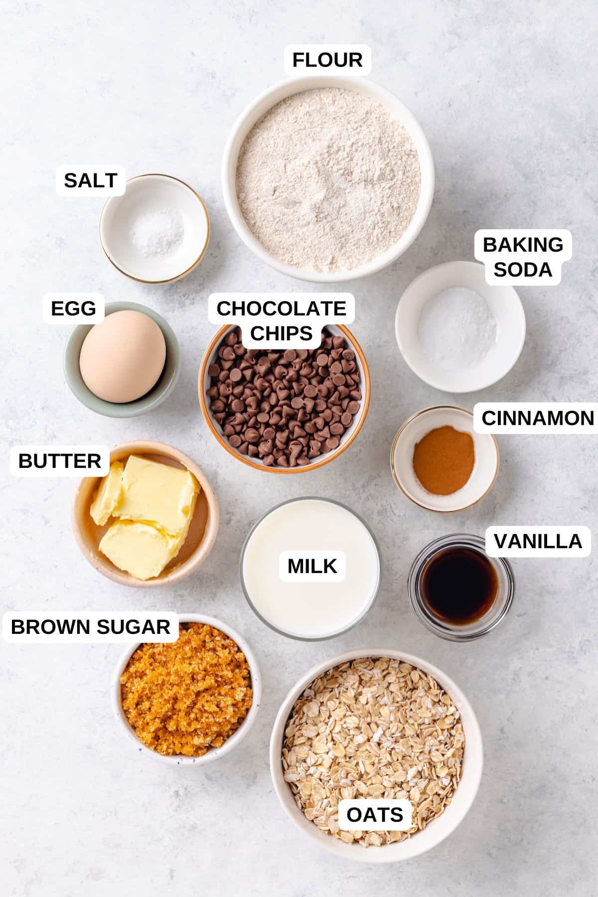 Ingredients laid out in separate bowls for making a chocolate chip muffin recipe with oats and flour.