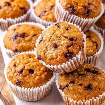 Close up of chocolate chip oatmeal muffins stacked on each other on a wood tray.