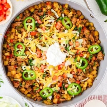 Close up of a large skillet with a a taco turkey and potato mixture with cheese, jalapeños, sour cream and pico on top.