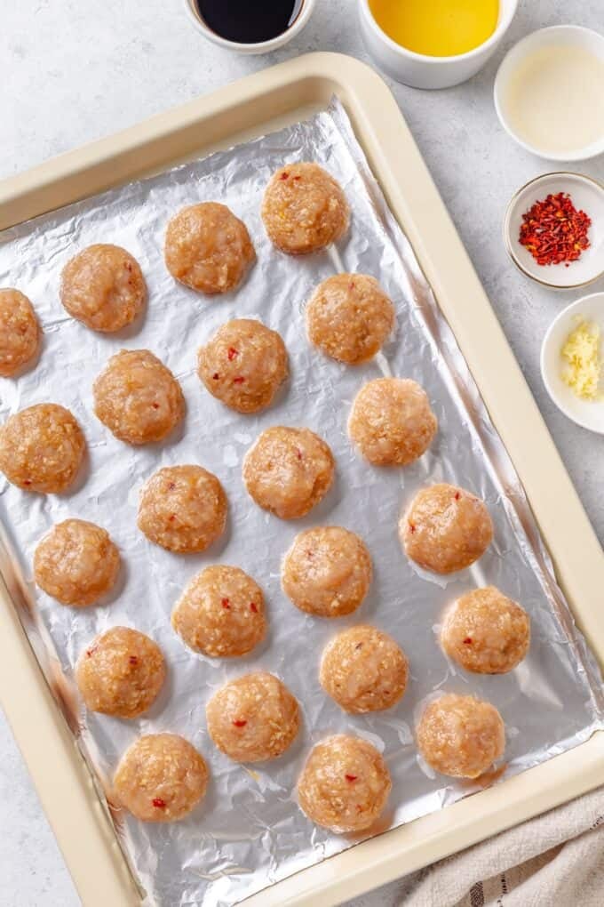 Rolled meatballs on a foil lined baking sheet before being baked.