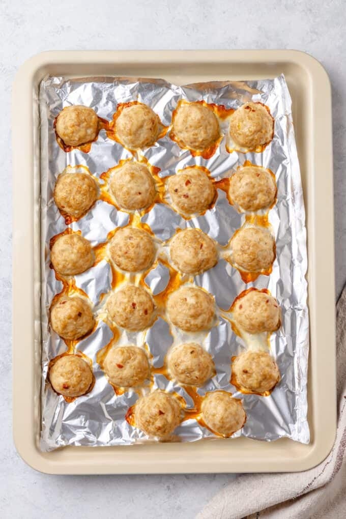 Baked meatballs on a foil lined baking sheet.