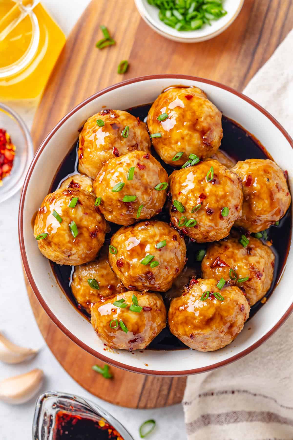 A bowl full of meatballs in a honey garlic sauce with sliced green onions sprinkled on top.