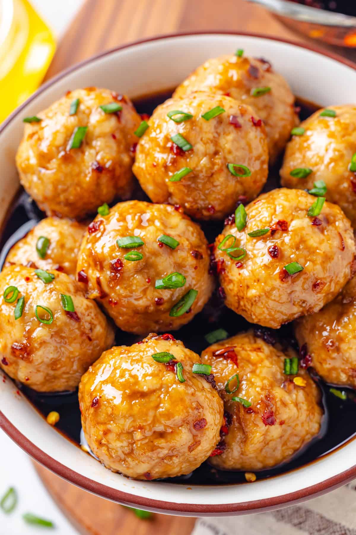 A bowl full of baked turkey meatballs in a honey garlic sauce with sliced green onions sprinkled on top.