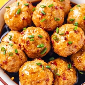 Close up of a bowl full of baked turkey meatballs in a honey garlic sauce with sliced green onions sprinkled on top.