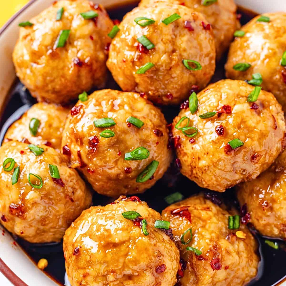 Close up of a bowl full of baked turkey meatballs in a honey garlic sauce with sliced green onions sprinkled on top.