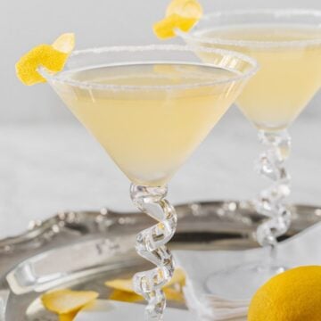 Close up of two martini glasses filled with a lemon drop martini, with sugared rims and lemon twists on the side.