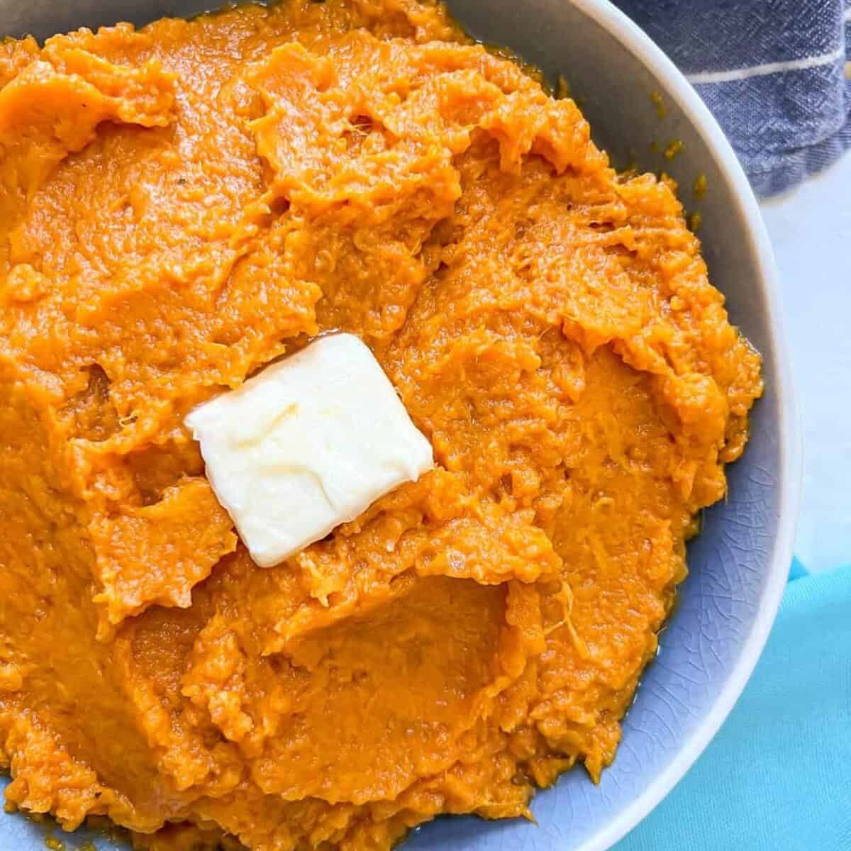 Close up of creamy mashed sweet potatoes in a blue serving bowl with a pat of butter on top