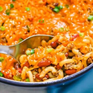 Close up of a serving spoon scooping up cheesy turkey chili mac from a large pot.