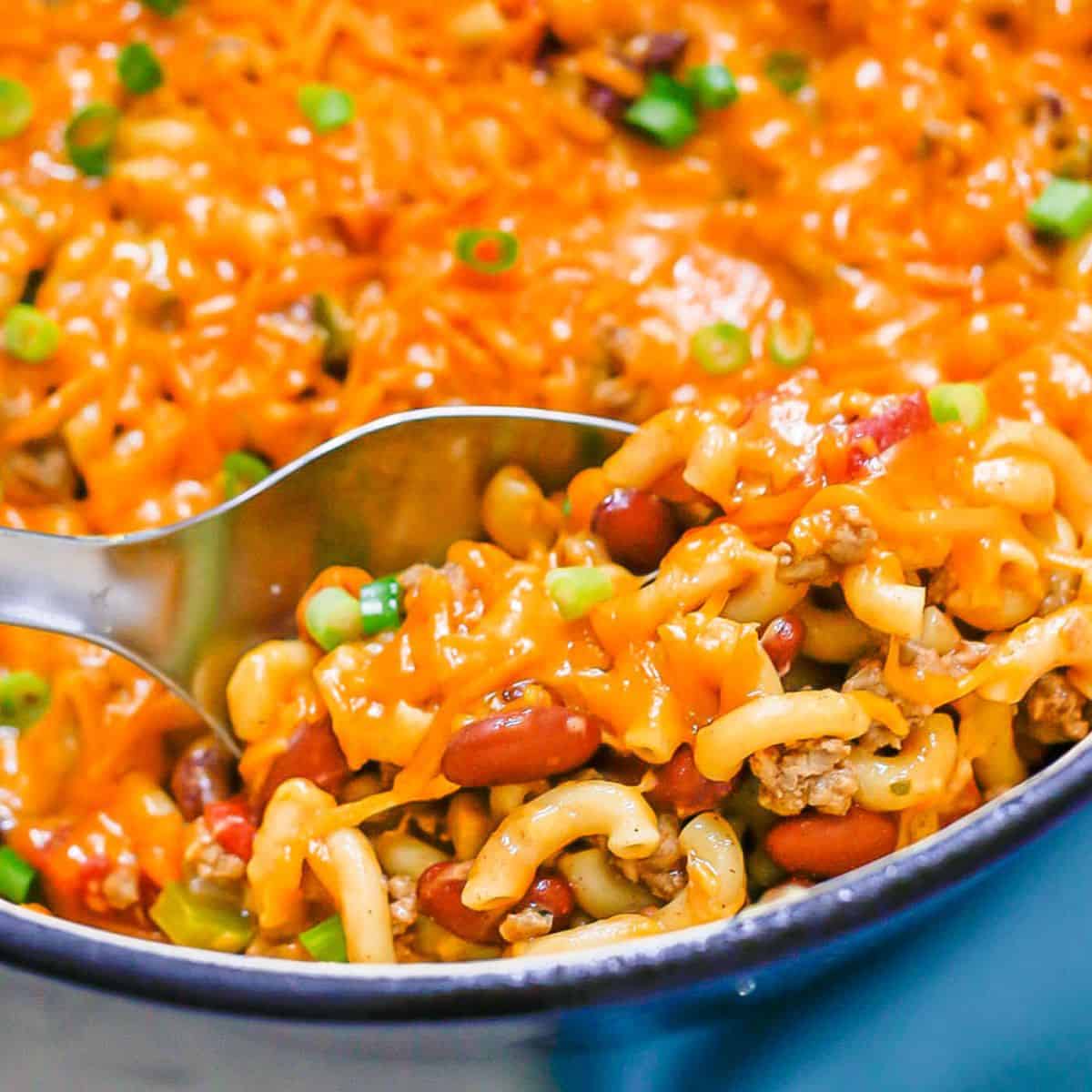 Close up of a serving spoon scooping up cheesy turkey chili mac from a large pot.