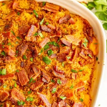 Close up of a baked macaroni and cheese with pumpkin and bacon in a white casserole dish.