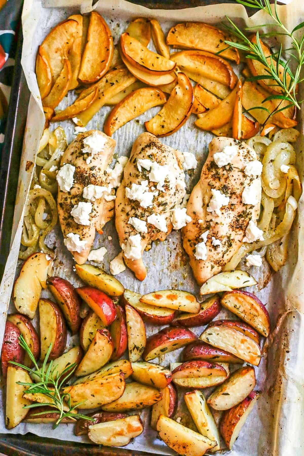 Sheet pan chicken and apples with potatoes is seasoned with fresh rosemary and finished with creamy goat cheese for a delicious and easy fall dinner. A sheet pan with chicken breasts topped with goat cheese in the middle and roasted apples to one side and roasted potato wedges to the other side with sprigs of fresh rosemary as garnish.