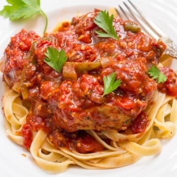 Close up of a low dinner bowl with fettuccine noodles topped with a slow cooker pork chop in a rich, thick tomato sauce.