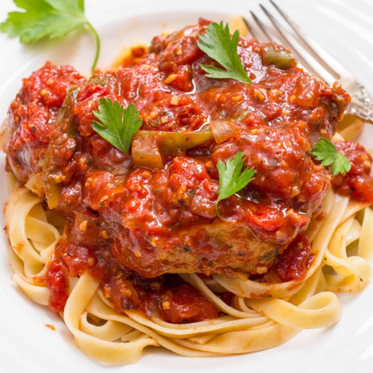 Close up of a low dinner bowl with fettuccine noodles topped with a slow cooker pork chop in a rich, thick tomato sauce.