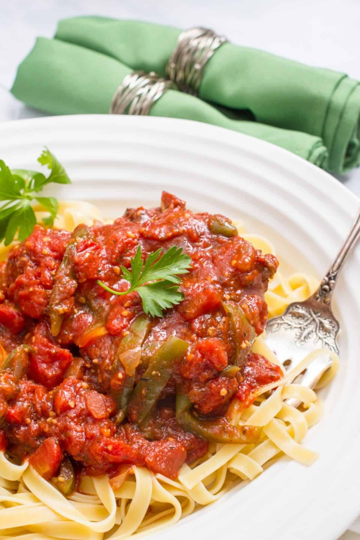 A serving bowl with fettuccine noodles topped with slow cooker pork chops in a rich, thick tomato sauce.
