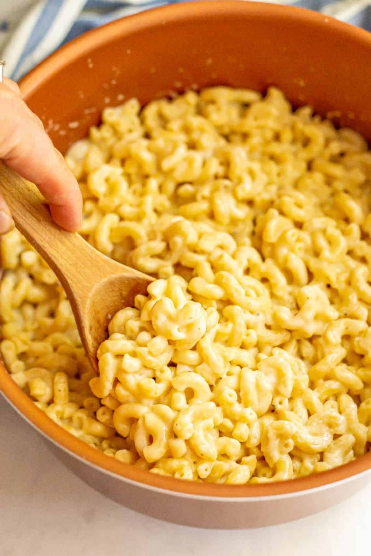 Easy stovetop mac and cheese is just 5 ingredients and 15 minutes to make, but so creamy, cheesy and delicious! It's perfect for an easy dinner side dish! #macandcheese #pasta #pastarecipes #easyrecipes A hand using a wooden spoon to scoop out some homemade mac and cheese from a large pot.