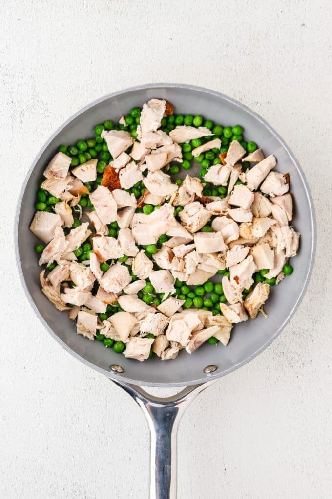 A skillet filled with rotisserie chicken pieces and green peas being warmed through.