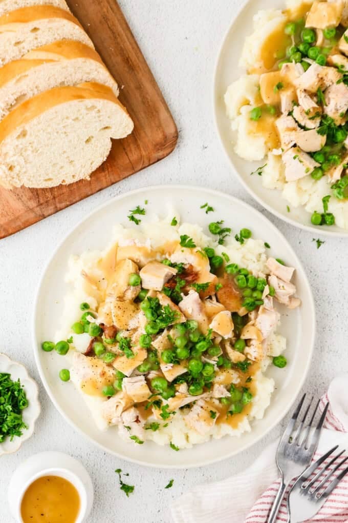 Dinner plates filled with mashed potatoes topped with chicken and peas and drizzled with gravy.