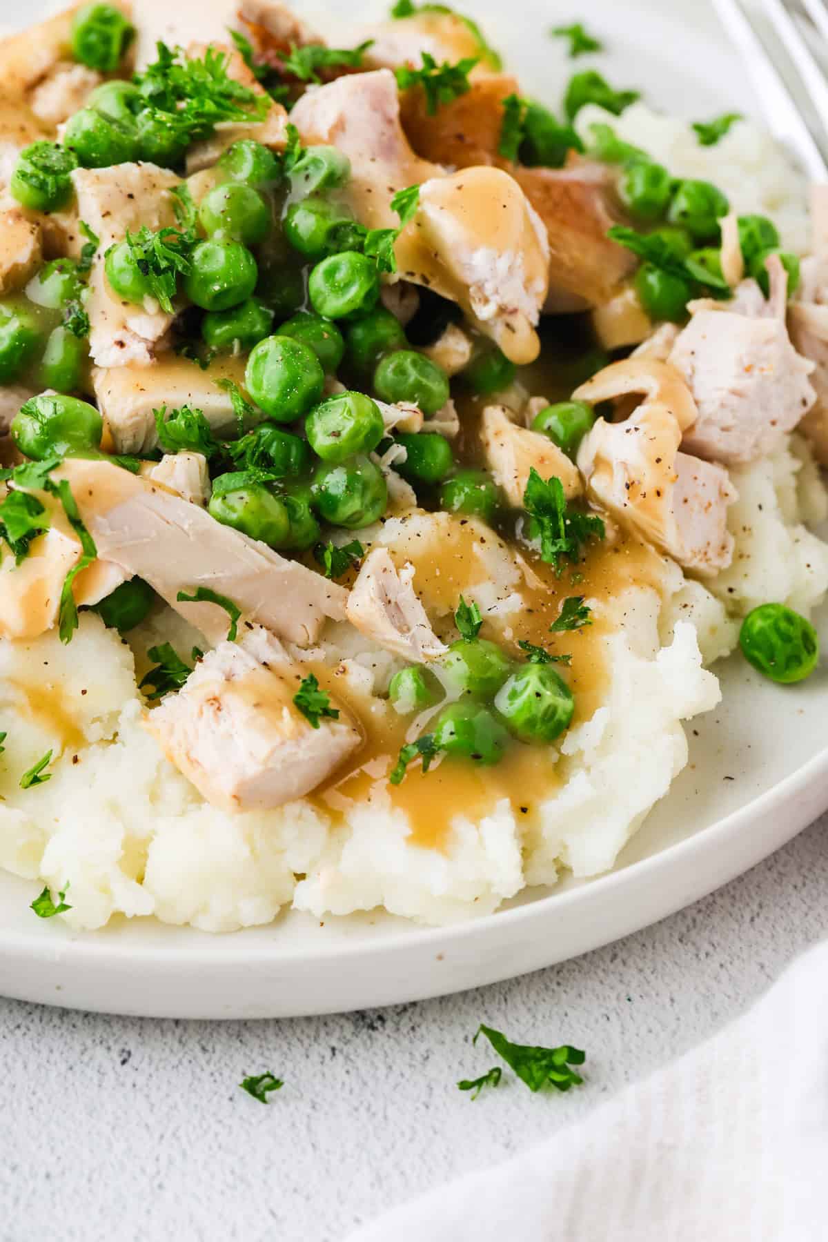 Close up of a mashed potato bowl with chicken and green peas and gravy.