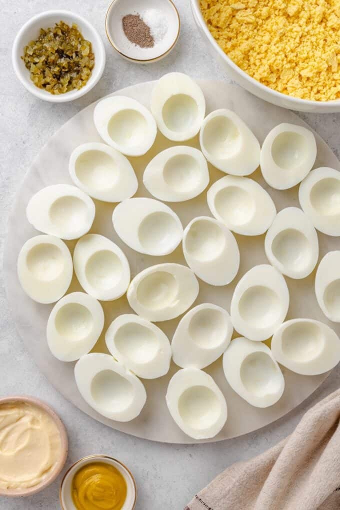 Empty egg white halves on a marble platter after the yolks have been scooped out into a bowl and crumbled.