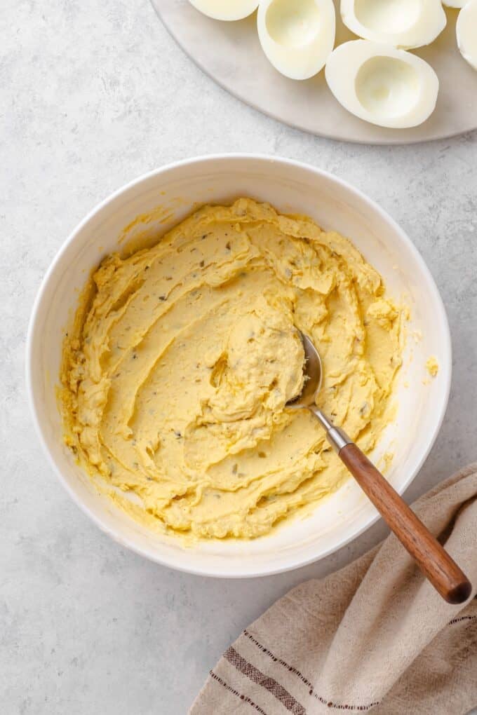 The deviled egg filling mixed until smooth and creamy in a white bowl with a wooden-handled spoon.