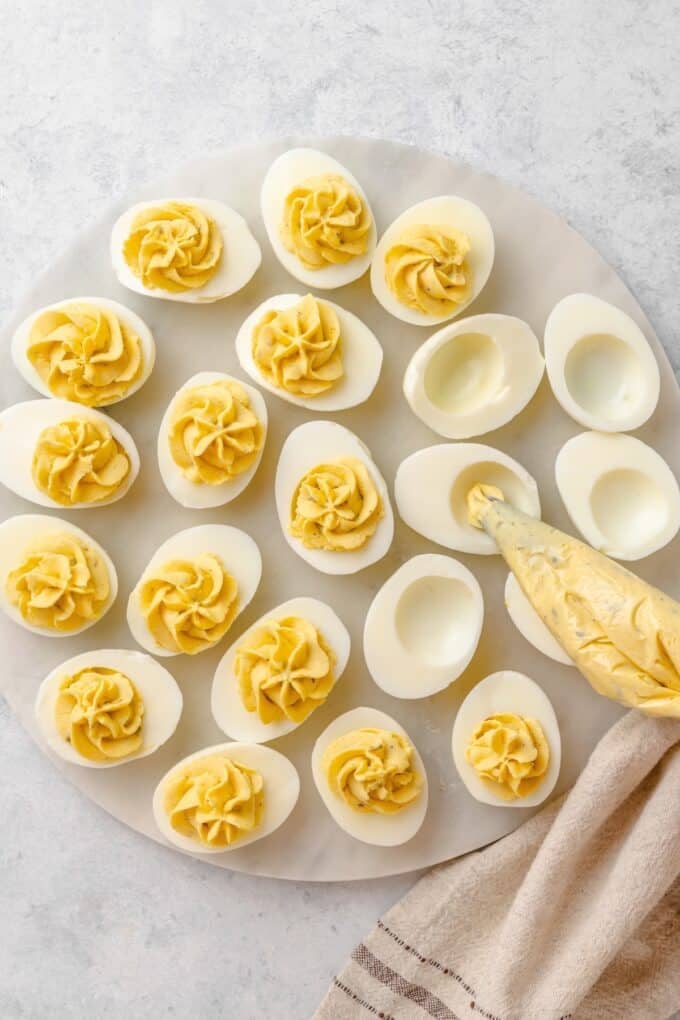 Piping the yolk filling into the egg white halves with a pastry bag, with about half of the eggs already filled.