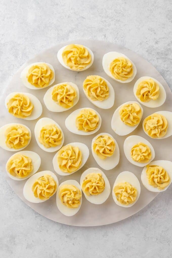 A round marble platter of filled deviled eggs, each with a piped swirl of creamy yolk filling.