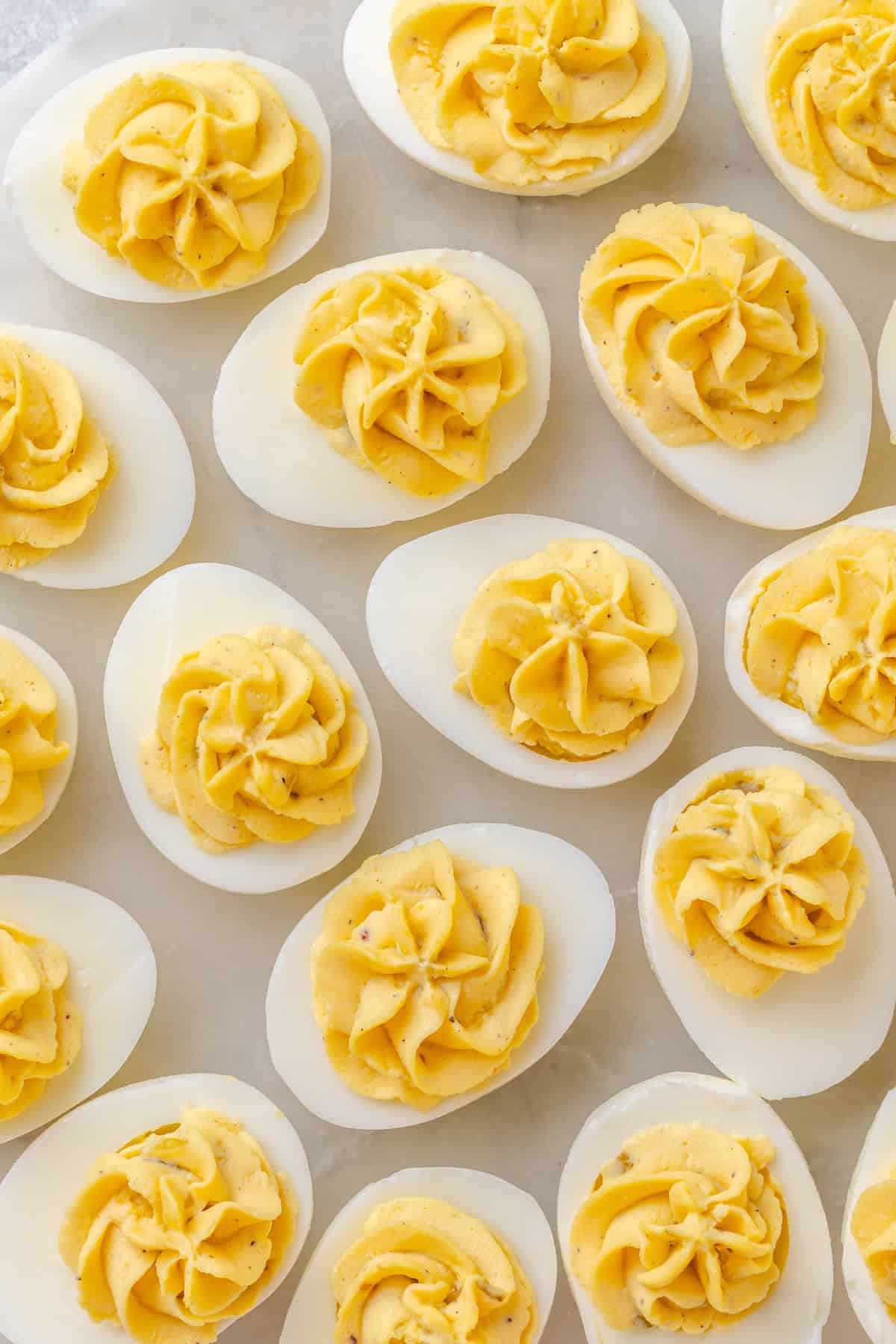 Close-up of deviled eggs with piped swirls of yellow filling flecked with black pepper and bits of sweet relish.