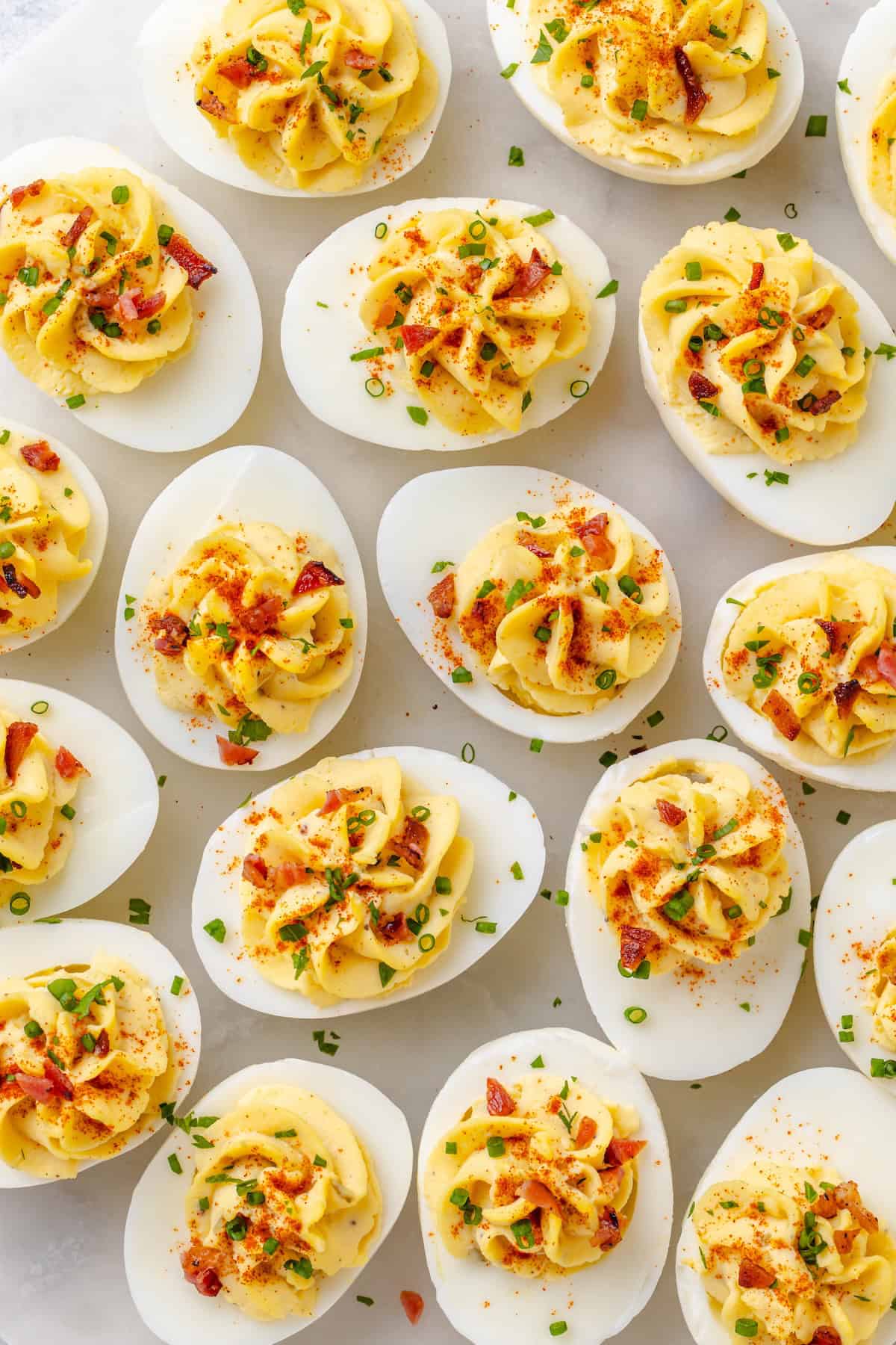 Overhead view of deviled eggs topped with crumbled bacon, snipped chives, and a sprinkle of paprika.