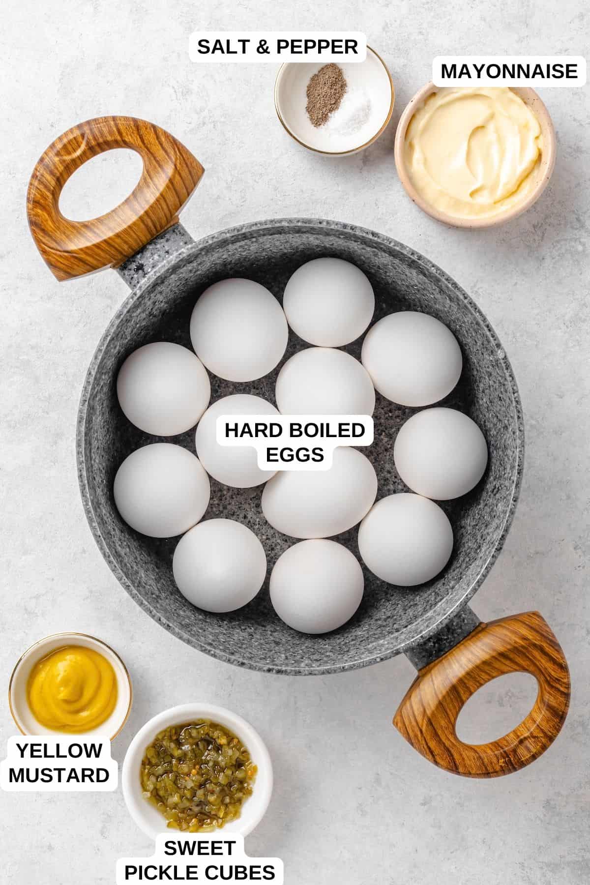 Ingredients for Southern deviled eggs: a pot of a dozen hard boiled eggs, with small bowls of mayonnaise, yellow mustard, sweet pickle cubes, and salt and pepper, each labeled.