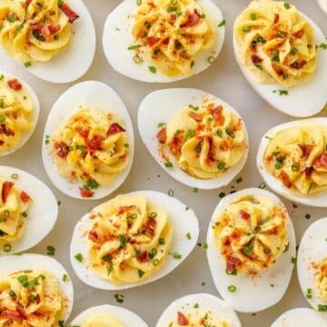 Overhead close-up of deviled eggs topped with crumbled bacon, chives, and paprika.