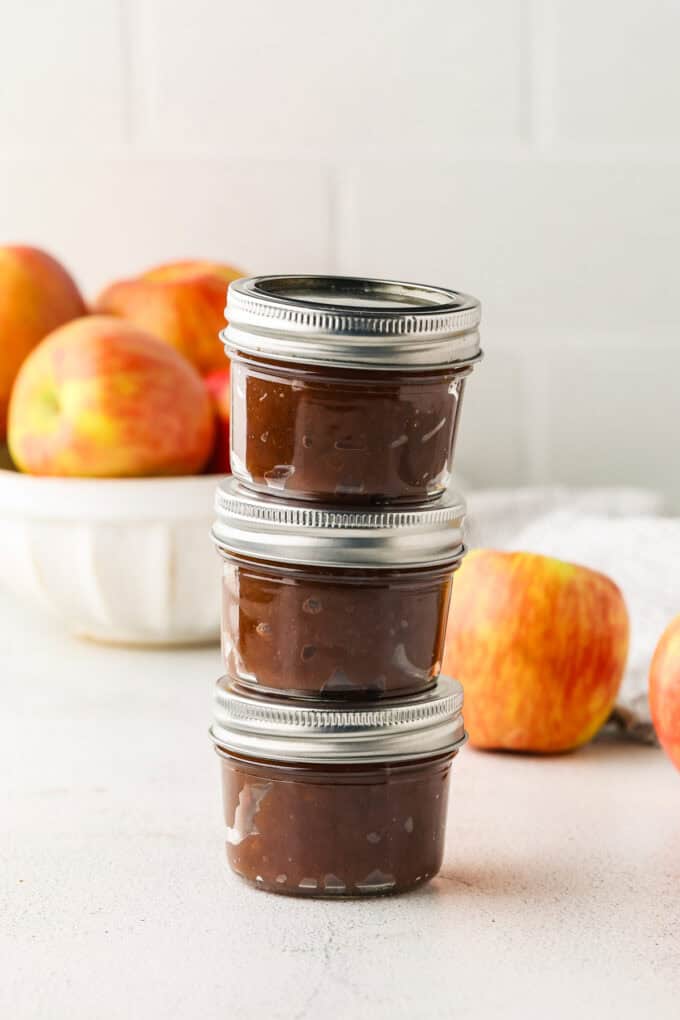 A trio of small glass jars filled with spiced apple butter stacked on each other.