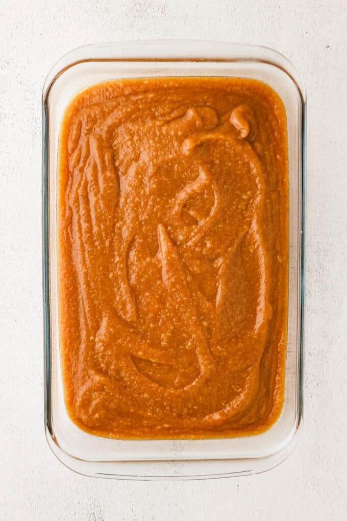 Smooth apple butter spread out in a glass casserole dish before being slow baked.